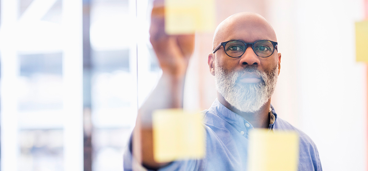 Portrait of businessman taking adhesive note from glass wall in office